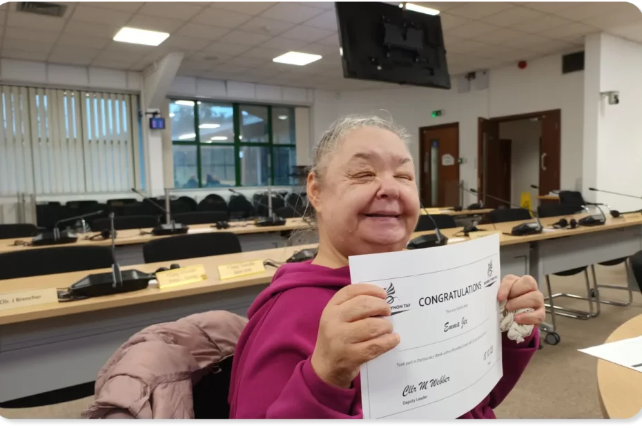 Emma smiling with a certificate from Rhondda Cynon Taf, attending a session about voting with a learning disability
