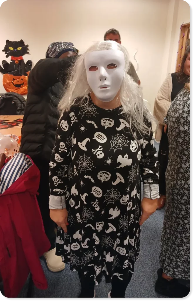 Natalie, dressed in a halloween themed dress, wearing a white mask on her face and a long white wig
