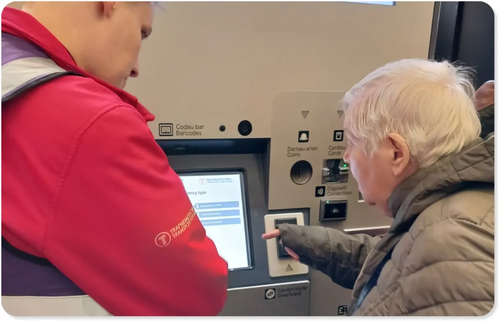 A person with a learning disability using a ticket machine at Cardiff Central train station with the assistance of a Transport for Wales staff member