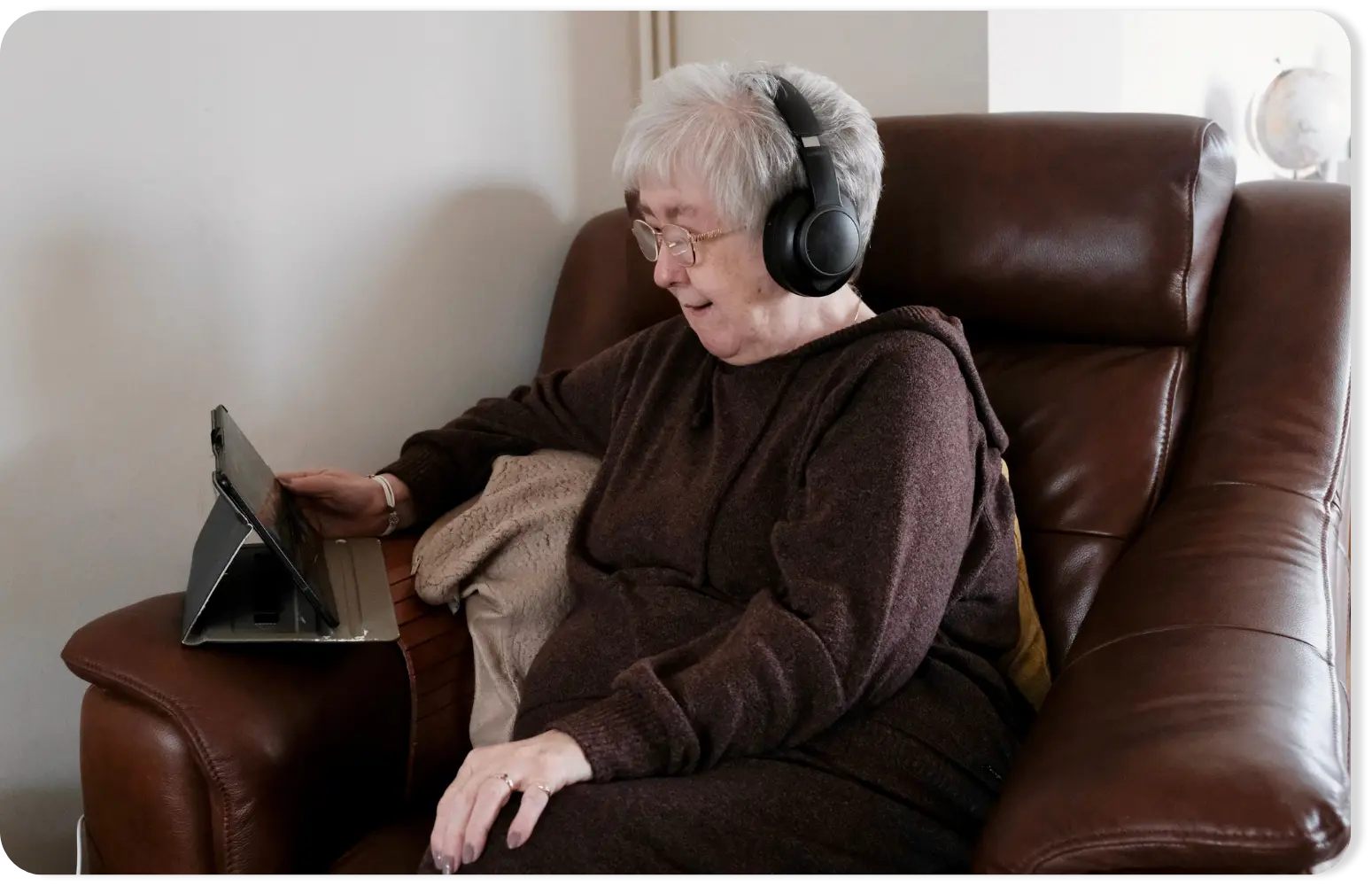 A person sitting in a brown armchair wearing headphones and using Insight app on a tablet on a stand.